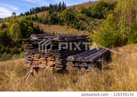 Wooden Stacks and Logs in the Hills: A Serene Landscape of Nature's Beauty and Timber Storage in Autumn Colors with Evergreen Trees Surrounding the Scene Wooden Stacks and Logs in the Hills: A Serene Landscape of Nature's Beauty and Timber Storage in Autumn Colors with Evergreen Trees Surrounding the Scene 128330130