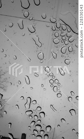 An Atmospheric Black and White Capture of Raindrops on a Window with a Glistening Texture and a Gloomy Sky as the Backdrop Creates a Moody Aesthetic Experience 128330143