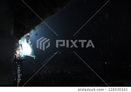 Nighttime Scene with Dramatic Lighting and Falling Snowflakes Captured in a Dark Environment Featuring a Bright Spotlight 128330161