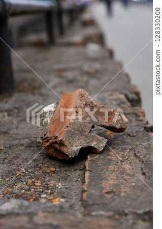 A Singular Fragment: The Beauty of a Weathered Brick Piece Set Against an Urban Landscape and Stone Pathway Captures the Essence of Time and Nature's Erosion in an Artistic Way 128330200