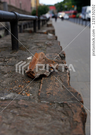 A Detailed Close-Up of a Fragment of Stone Resting on a Cracked Stone Surface Alongside a Sidewalk with Blurred Background, Urban Scene and Traffic Indicators Visible 128330202