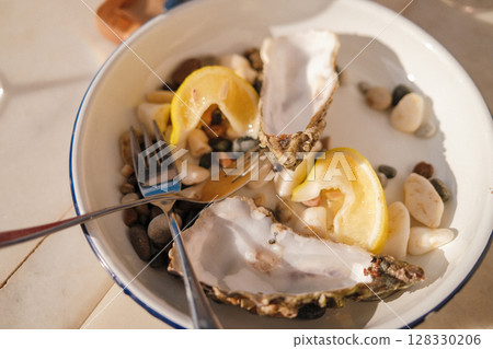 Fresh oysters on ceramic plate with lemon wedges served for gourmet dining Fresh oysters on ceramic plate with lemon wedges served for gourmet dining 128330206