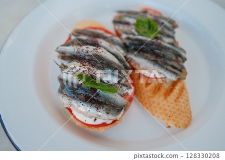 Open-faced sandwich with sprats, fresh tomato slices, mozzarella on white plate 128330208