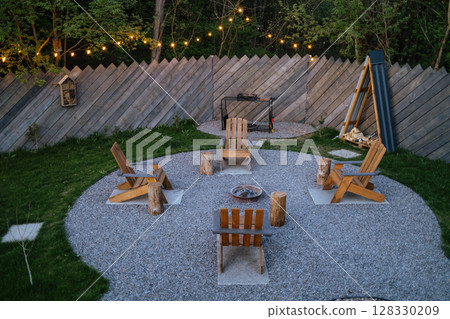 Cozy backyard fire pit area with wooden chairs, string lights, evening gathering 128330209