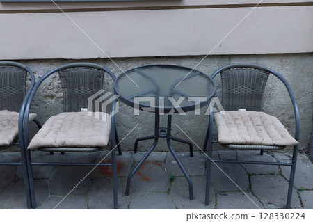 A Cozy Outdoor Caf Scene Featuring Three Stylish Metal Chairs with Cushions and a Glass-Top Table, Perfect for Relaxation or Enjoying a Beverage in a Charming Setting 128330224