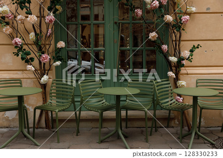 Charming Outdoor Caf Scene Featuring Green Tables, Modern Chairs, and Beautiful Floral Arrangements Against a Stylish Backdrop of Warm Earthy Tones and Elegant Green Window Charming Outdoor Caf Scene Featuring Green Tables, Modern Chairs, and Beautiful Floral Arrangements Against a Stylish Backdrop of Warm Earthy Tones and Elegant Green Window 128330233