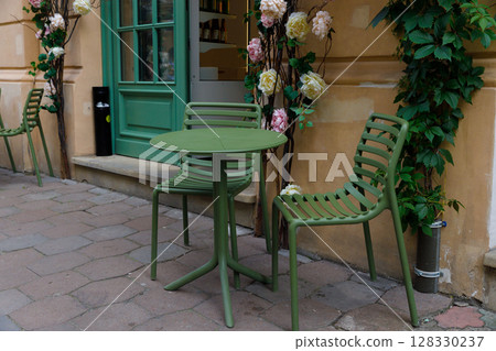 Charming Outdoor Caf Scene Featuring Green Seating and Floral Accents, Ideal for a Relaxing Afternoon in a Lively Urban Setting with Enticing Culinary Delights Nearby Charming Outdoor Caf Scene Featuring Green Seating and Floral Accents, Ideal for a Relaxing Afternoon in a Lively Urban Setting with Enticing Culinary Delights Nearby 128330237