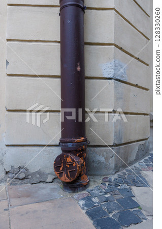 Urban architectural detail showcasing a brown drainage pipe on the corner of a building, revealing weathered paint and textured walls that contribute to the city's character and history. Urban architectural detail showcasing a brown drainage pipe on the corner of a building, revealing weathered paint and textured walls that contribute to the city's character and history. 128330260