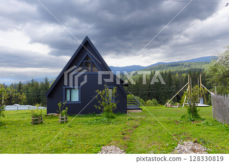 Charming Black Cabin Surrounded by Lush Greenery and Mountain View, Ideal for Relaxation and Nature Retreat in the Countryside Under a Dramatic Cloudy Sky Charming Black Cabin Surrounded by Lush Greenery and Mountain View, Ideal for Relaxation and Nature Retreat in the Countryside Under a Dramatic Cloudy Sky 128330819