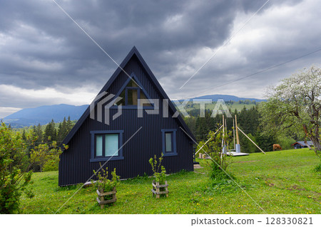 Scenic View of a Modern A-Frame House Surrounded by Lush Greenery and Mountainous Landscape Under a Dramatic Cloudy Sky 128330821