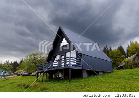Modern A-Frame House Surrounded by Lush Greenery Under Dramatic Grey Skies, Perfectly Blending Nature with Contemporary Architecture in a Serene Setting 128330832