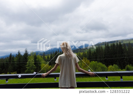 A Serene Mountain Getaway: A Young Woman Enjoys the Peaceful Beauty of a Cloudy Day Surrounded by Lush Forests and Majestic Mountains in This Scenic Landscape 128331222