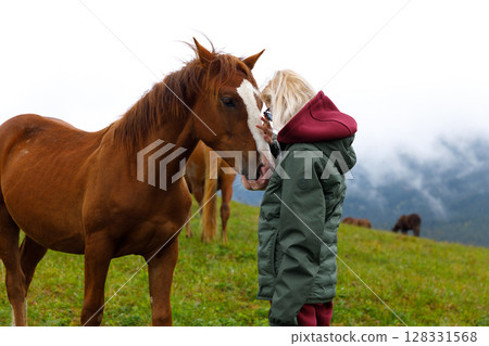 A Young Girl Bonds with a Beautiful Chestnut Horse in a Lush Green Field Under a Cloudy Sky, Embracing the Beauty of Nature and the Joy of Connection with Animals A Young Girl Bonds with a Beautiful Chestnut Horse in a Lush Green Field Under a Cloudy Sky, Embracing the Beauty of Nature and the Joy of Connection with Animals 128331568