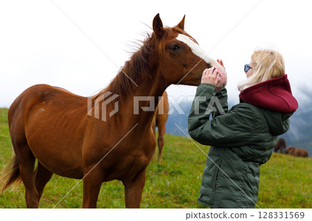 Embracing the Bond: A Heartwarming Interaction Between a Woman and a Gracious Horse Amidst a Beautiful Natural Landscape on a Cloudy Day Embracing the Bond: A Heartwarming Interaction Between a Woman and a Gracious Horse Amidst a Beautiful Natural Landscape on a Cloudy Day 128331569