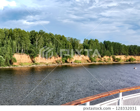 Dramatic scene of dark thunderclouds over a pine forest on a riverbank, viewed from the side of a ship Dramatic scene of dark thunderclouds over a pine forest on a riverbank, viewed from the side of a ship 128332031