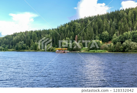 View from the river to a small pier on the other bank, with a coniferous forest in the background, on a summer day View from the river to a small pier on the other bank, with a coniferous forest in the background, on a summer day 128332042