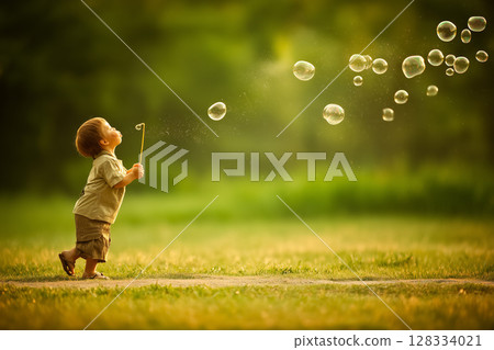 Cheerful Child Blowing Soap Bubbles in a Sunny Green Field, Capturing Joyful Childhood Moments 128334021