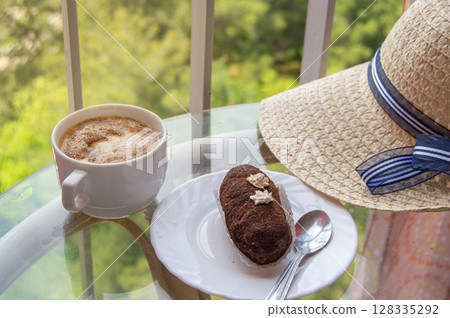 Vintage still life with a woman's hat, a cup of coffee and a brownie on a glass table 128335292