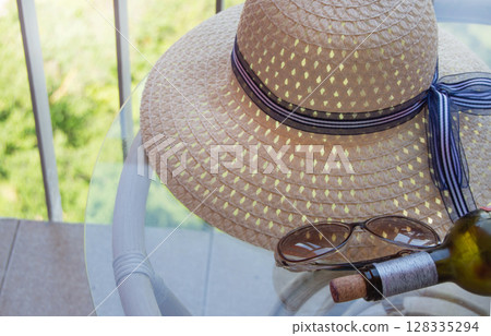 A woman's summer hat, an empty bottle of wine and sunglasses on a clear glass table on the balcony. Vacation concept 128335294