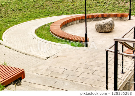 Close-up of a wooden bench and an arc-shaped sidewalk in a city park on a sunny summer day 128335298