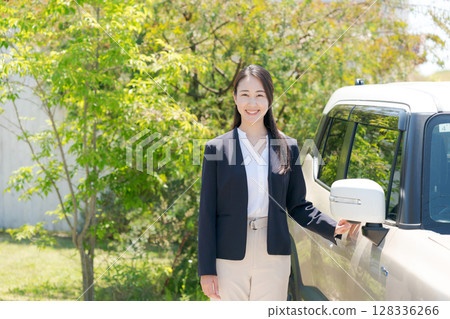 一名身穿西裝的女子站在一輛汽車旁 一名身穿西裝的女子站在一輛汽車旁 128336266