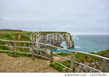 Etretat cliff arch seen from coastal trail with railing Etretat cliff arch seen from coastal trail with railing 128336280
