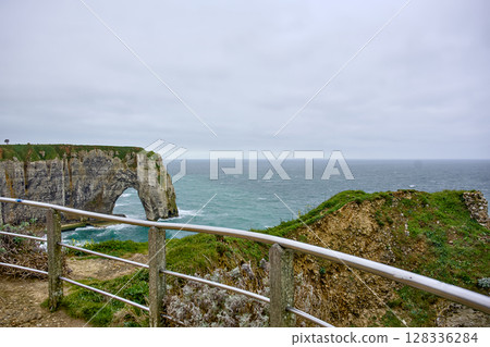 Ocean horizon and Etretat cliff arch seen from fenced trail 128336284