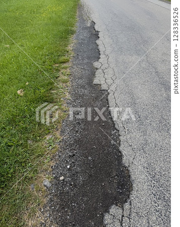 Road with a crack in it and grass growing on the side 128336526