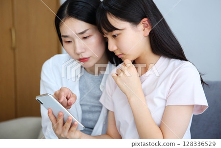 Image of a mother and daughter looking seriously at a smartphone 128336529