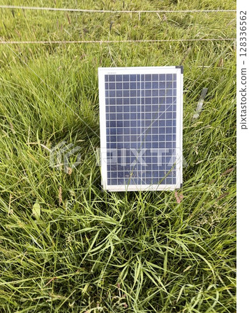 Solar panel is sitting on a grassy field 128336562
