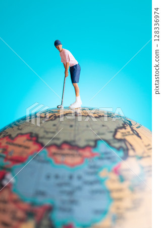 A miniature figure of a golfer playing on top of a globe 128336974
