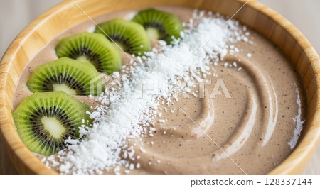 Smoothie Bowl with Kiwi Fruit Slices and Coconut Shavings in Wooden Bowl 128337144