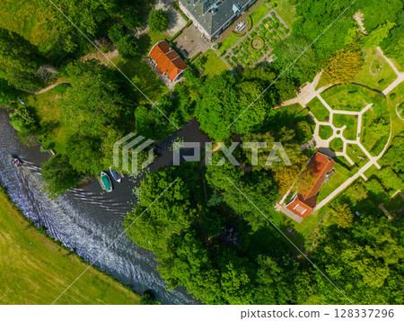 Aerial view of a symmetrical garden with pathways, green hedges, and red-roofed buildings surrounded by dense trees. A perfect blend of nature and architecture in a peaceful estate. Aerial view of a symmetrical garden with pathways, green hedges, and red-roofed buildings surrounded by dense trees. A perfect blend of nature and architecture in a peaceful estate. 128337296