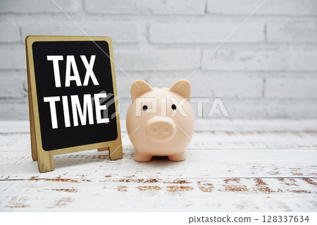 Tax Time text message and piggy saving on wooden and white brick wall background (Business concept) 128337634