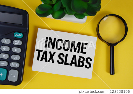 Income Tax Slabs text with magnifying glass anc calculator on yellow background 128338106