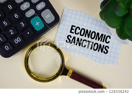 Economic Sanctions text with magnifying glass anc calculator on yellow background 128338242