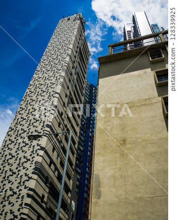 A tall skyscraper with a black and white pattern on the facade stands against a blue sky. 128339925