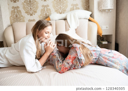 Women Bedroom Relaxation: Two young women sharing intimate moment, lying on bed in luxurious bedroom, enjoying peaceful time together. 128340305
