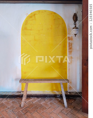 The white cement wall texture with yellow arched doorway and a wooden bench in front. 128340385