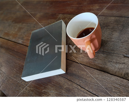 An unidentified book with a black cover placed next to a beige ceramic teacup on a wooden table. An unidentified book with a black cover placed next to a beige ceramic teacup on a wooden table. 128340387