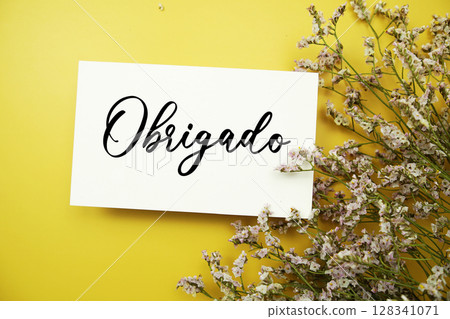 Obrigado (Portuguese Language) text with flowers decoration on yellow background Obrigado (Portuguese Language) text with flowers decoration on yellow background 128341071