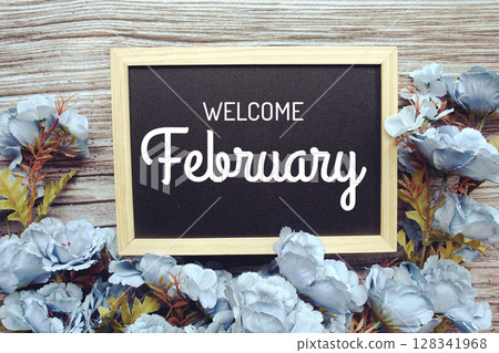 Welcome February text with flowers frame decoration top view on wooden background, 128341968