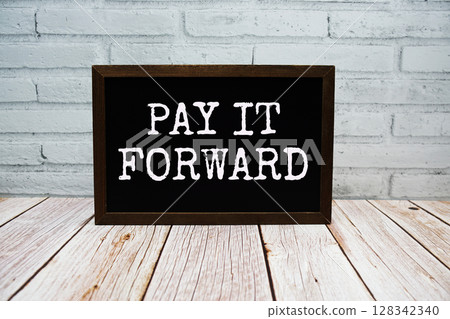Pay it forward text written on chalkboard standing on wooden background 128342340