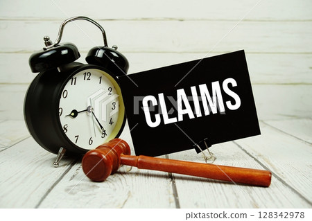 Claims text on paper card with alarm clock and wooden judge gavel on wooden background Claims text on paper card with alarm clock and wooden judge gavel on wooden background 128342978