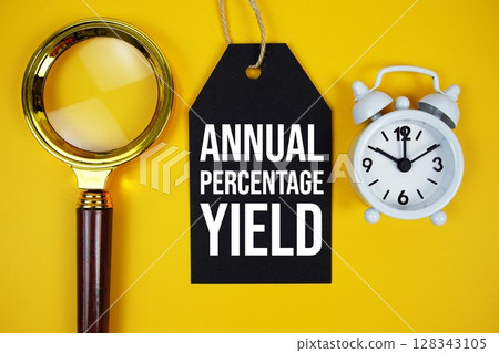 Annual Percentage Yield text on price tag with magnifying glass and alarm clock on yellow background 128343105