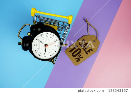 Sale 10% text on price tag with alarm clock and trolley shopping cart on pink, purple, blue geometric background 128343167