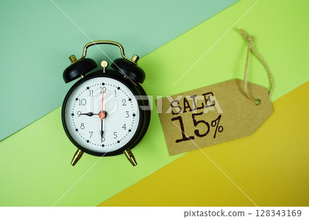 Sale 15% text on price tag with alarm clock and trolley shopping cart on green, yellow geometric background Sale 15% text on price tag with alarm clock and trolley shopping cart on green, yellow geometric background 128343169
