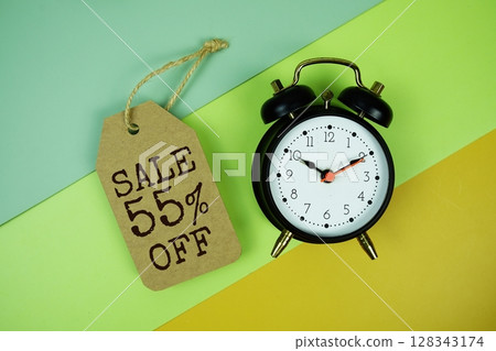 Sale 55% off text on price tag with alarm clock on green, yellow geometric background 128343174