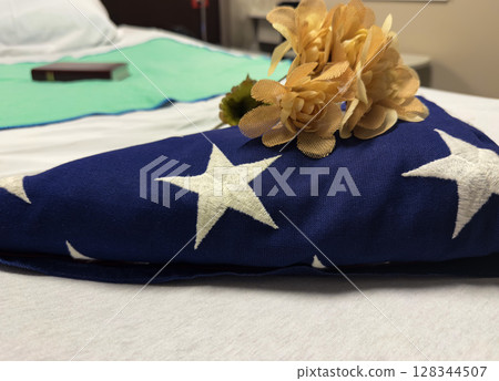 Folded Veteran Flag, Holy Bible, and Flowers on Hospice Bed Honoring End-of-Life 128344507