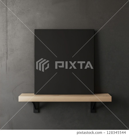 blank black canvas hanging on a wooden shelf against a gray concrete wall. The canvas is rectangular in shape and appears to be made of a light-colored wood	 128345544